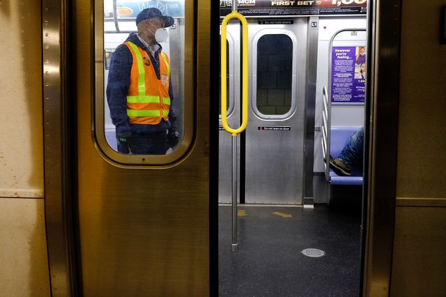 An MTA worker waits for a man lying down on an E train to join other riders on the platform at the end of the line in Jamaica, Queens.